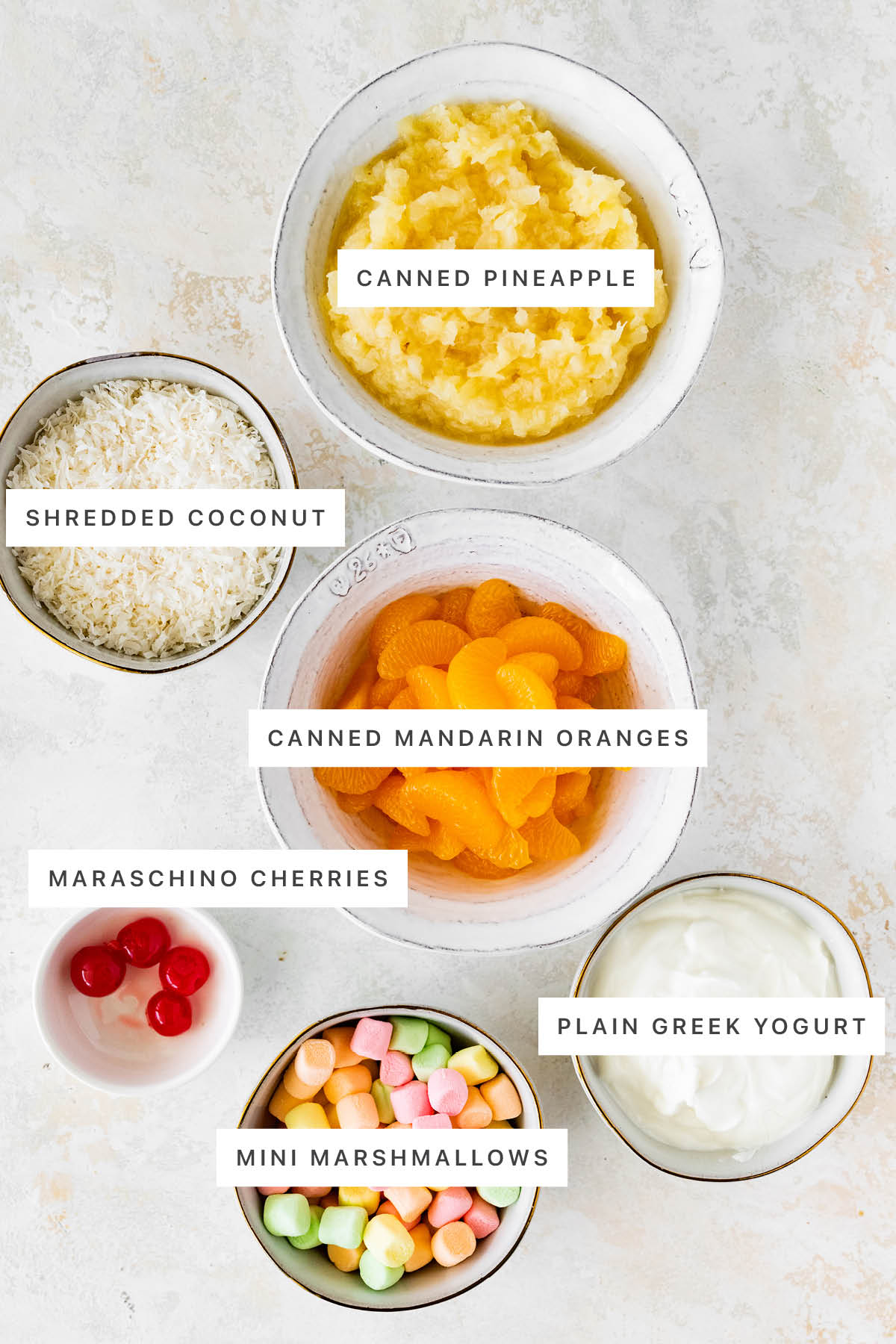 Ingredients measured out to make Healthy Ambrosia Salad: canned pineapple, shredded coconut, canned mandarin oranges, maraschino cherries, plain Greek yogurt and mini marshmallows.
