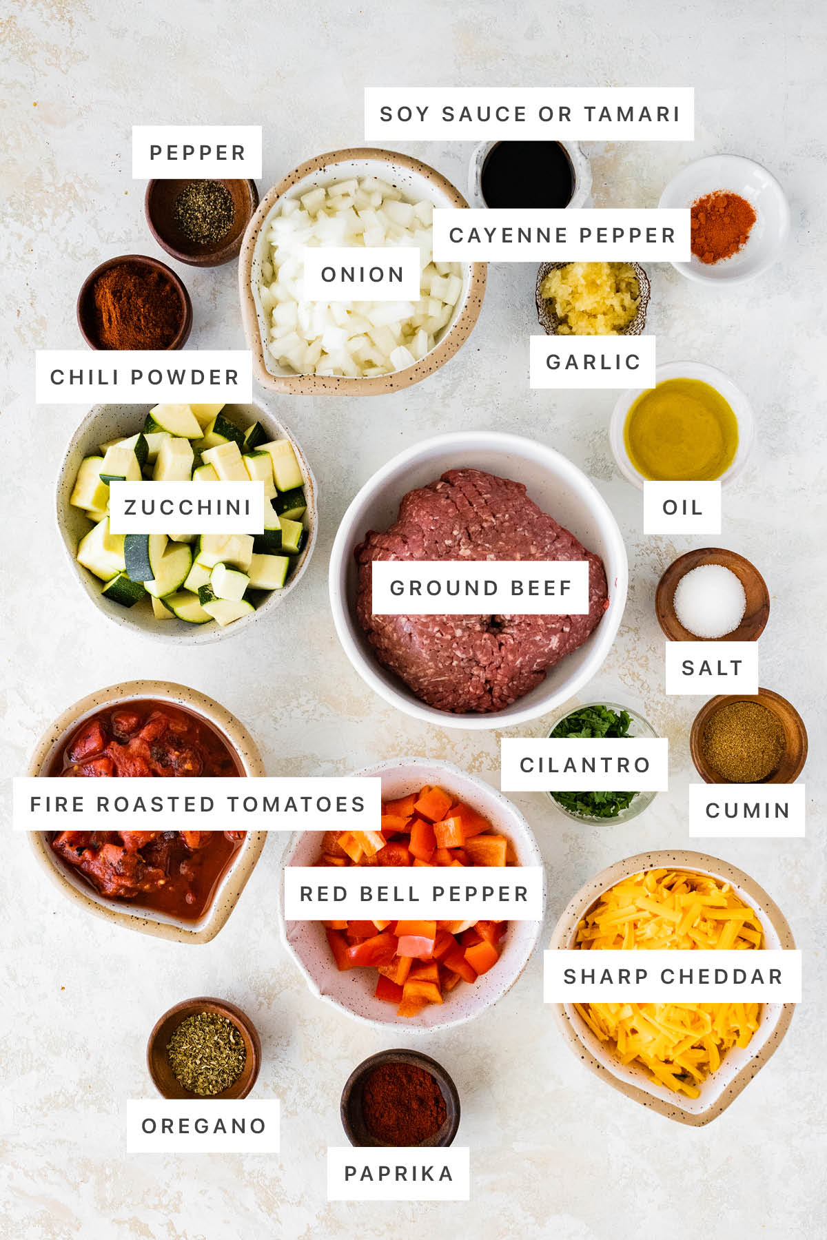 Ingredients measured out to make Ground Beef and Squash Skillet: pepper, soy sauce, cayenne pepper, onion, garlic, chili powder, zucchini, ground beef, oil, salt, cilantro, fire roasted tomatoes, red bell pepper, cumin, sharp cheddar, oregano and paprika.