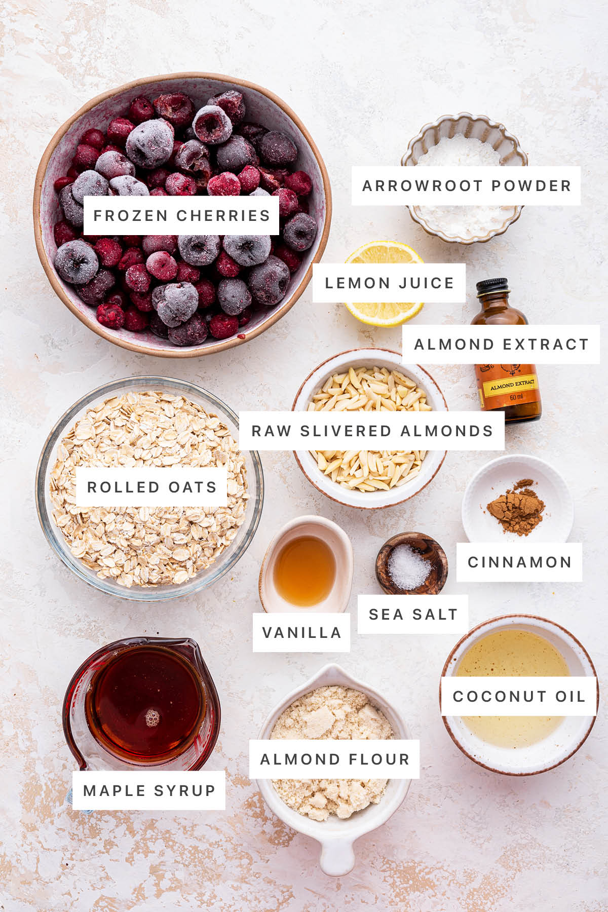 Ingredients measured out to make Healthy Cherry Crisp: frozen cherries, arrowroot powder, lemon juice, almond extract, raw slivered almonds, rolled oats, cinnamon, vanilla, sea salt, maple syrup, almond flour and coconut oil.