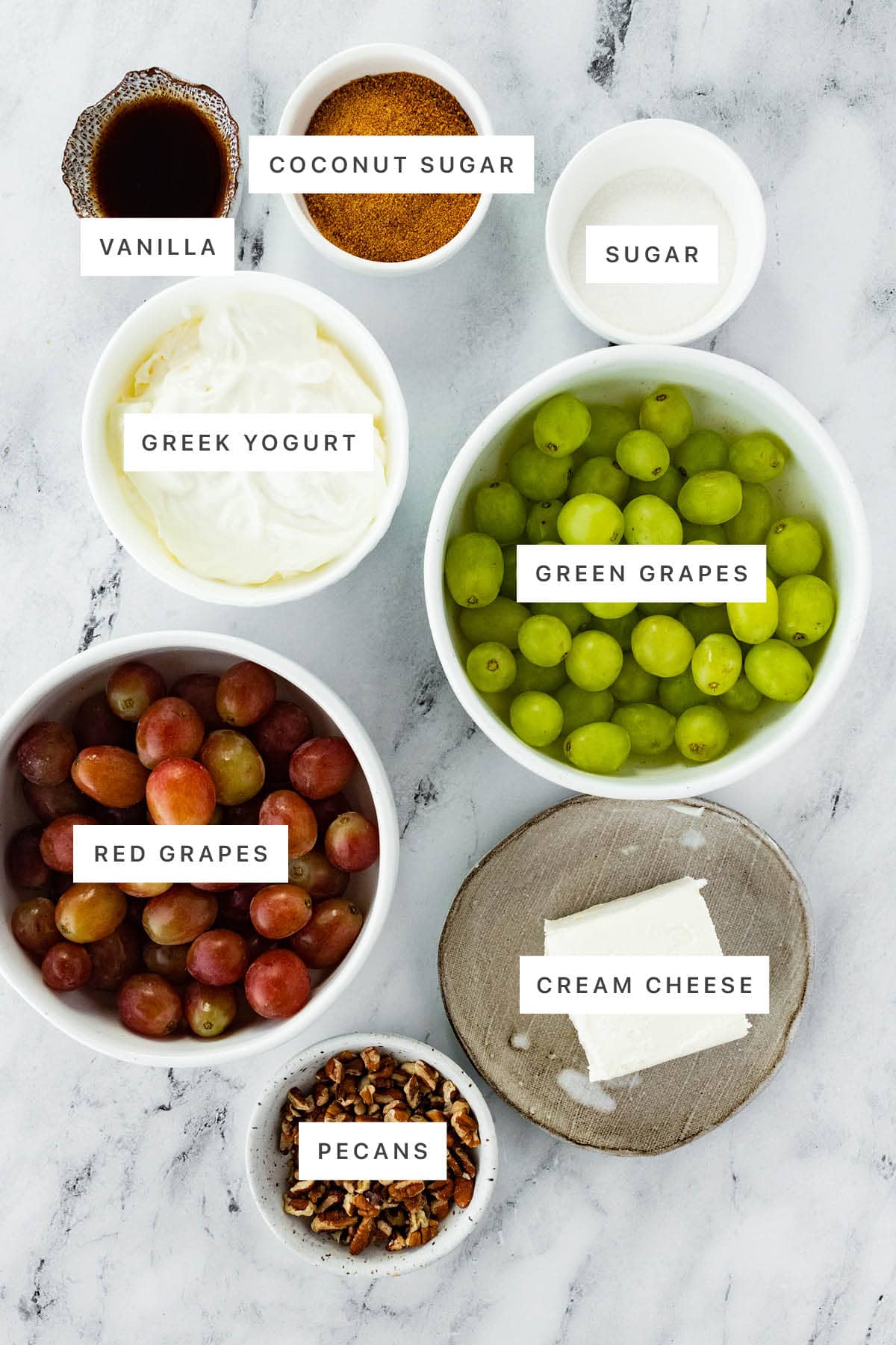 Ingredients measured out to make Creamy Grape Salad: vanilla, coconut sugar, sugar, Greek yogurt, green grapes, red grapes, cream cheese and pecans.