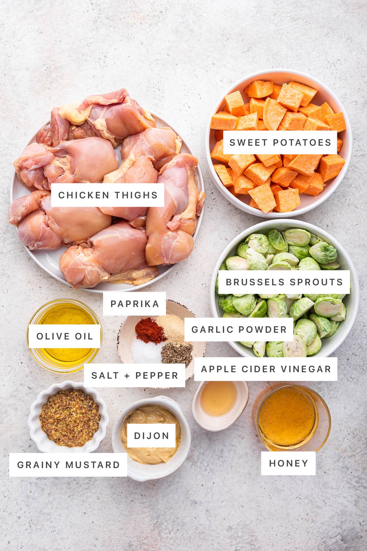 Ingredients measured out to make a Honey Mustard Chicken Sheet Pan Meal: chicken thighs, sweet potatoes, brussels sprouts, paprika, garlic powder, olive oil, salt, pepper, apple cider vinegar, grainy mustard, dijon and honey.
