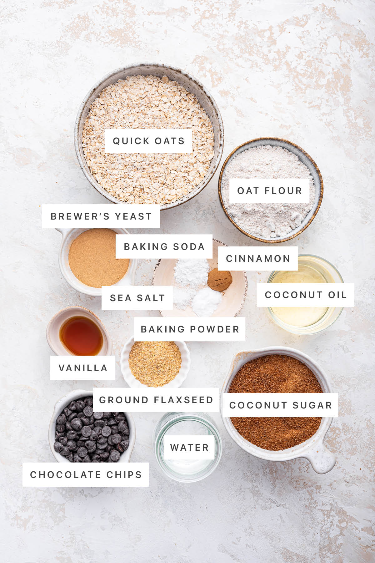 Ingredients measured out to make Healthy Lactation Cookies: quick oats, oat flour, brewer's yeast, baking soda, cinnamon, coconut oil, sea salt, baking powder, vanilla, ground flaxseed, chocolate chips, water and coconut sugar.