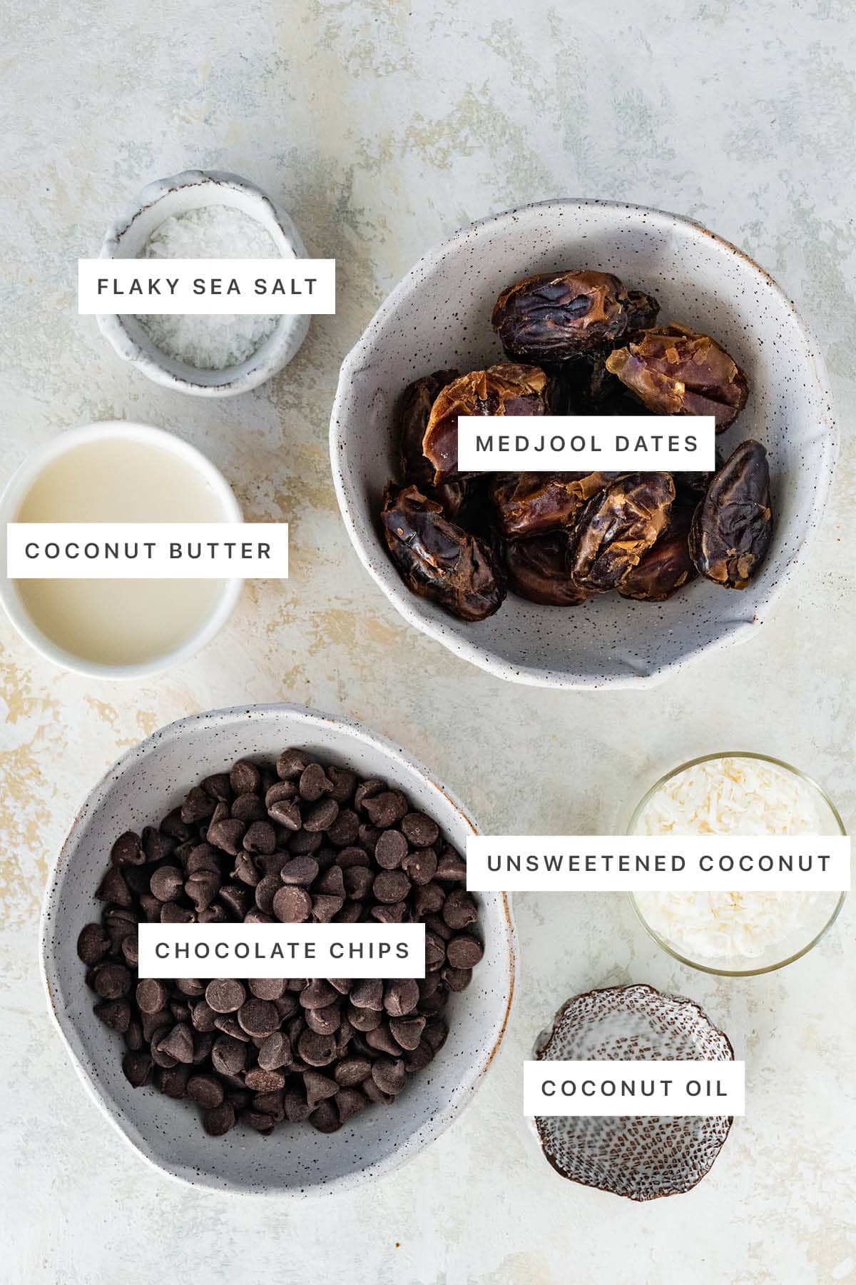 Ingredients measured out to make Date Mounds Bars: flaky sea salt, medjool dates, coconut butter, unsweetened coconut, chocolate chips and coconut oil.