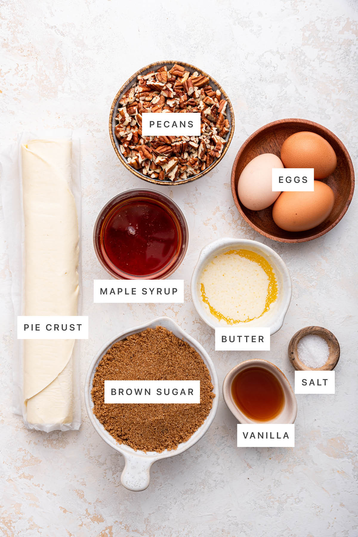 Ingredients measured out to make Easy Pecan Pie: pie curst, pecans, maple syrup, eggs, butter, brown sugar, vanilla and salt.