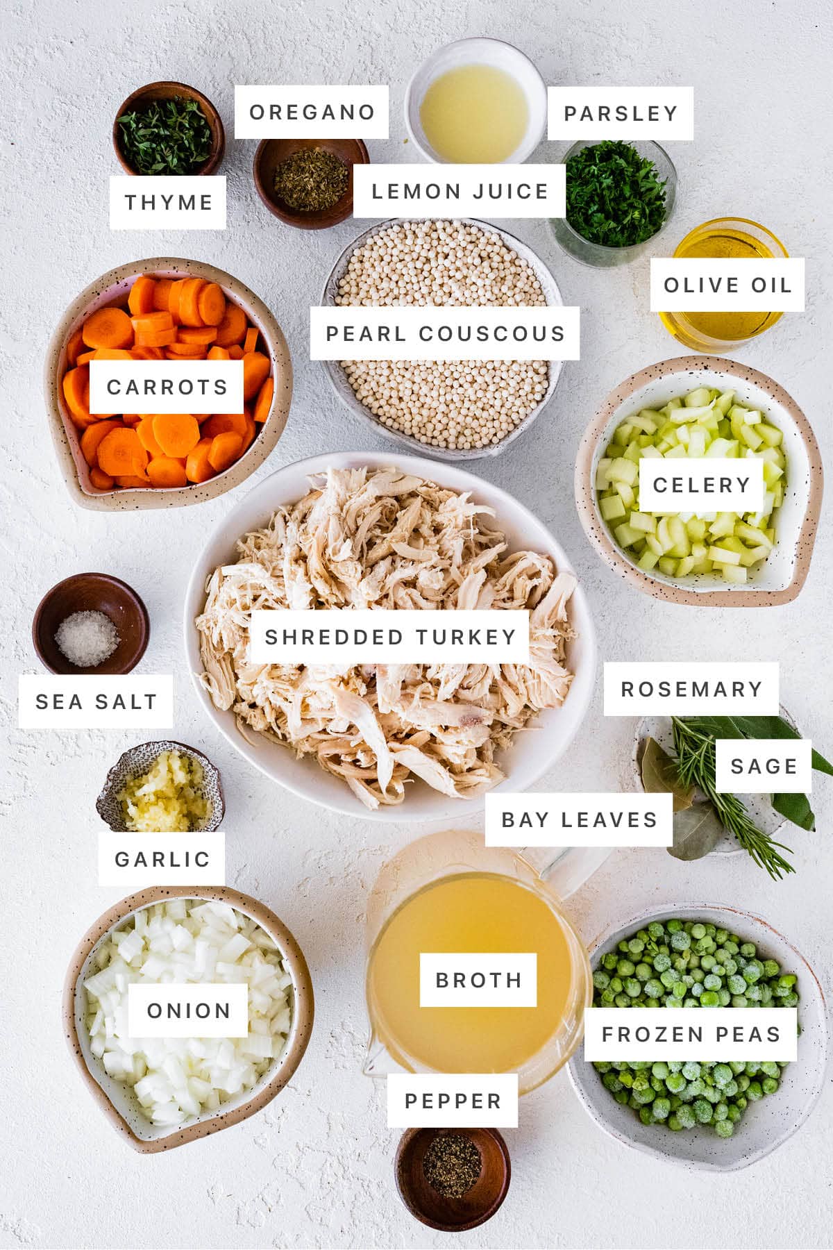 Ingredients measured out to make Turkey Soup: thyme, oregano, lemon juice, parsley, pearl couscous, carrots, olive oil, celery, sea salt, shredded turkey, rosemary, sage, bay leaves, garlic, onion, broth, pepper and frozen peas.