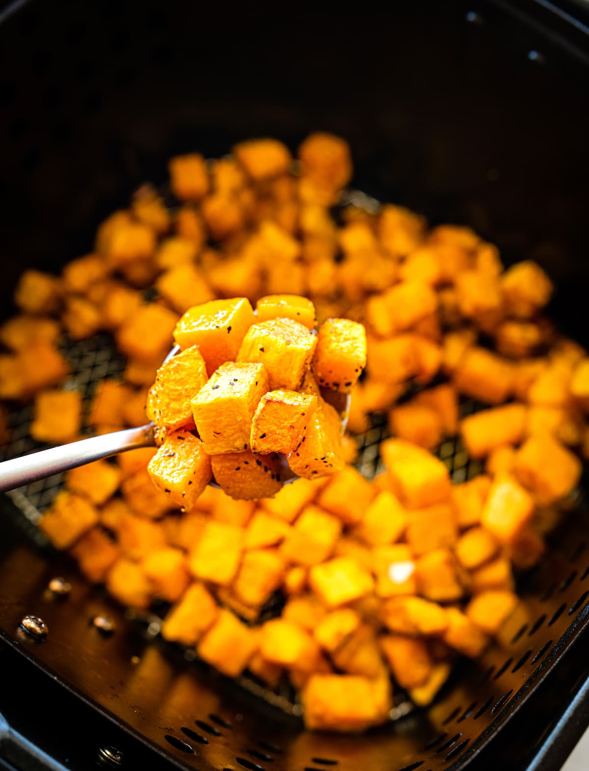 A metal spoon with a spoonful of cubed butternut squash that has been air fried.