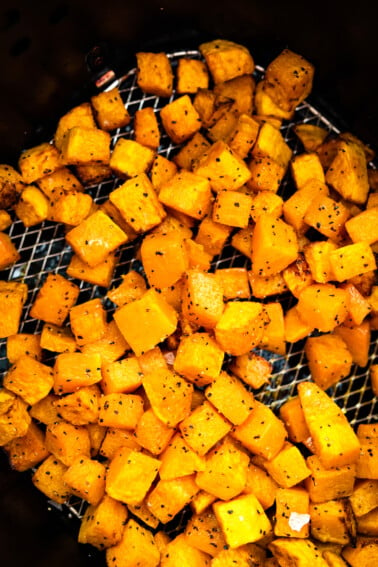 Cubed butternut squash that has been seasoned and is sitting in an air fryer basket in an air fryer.