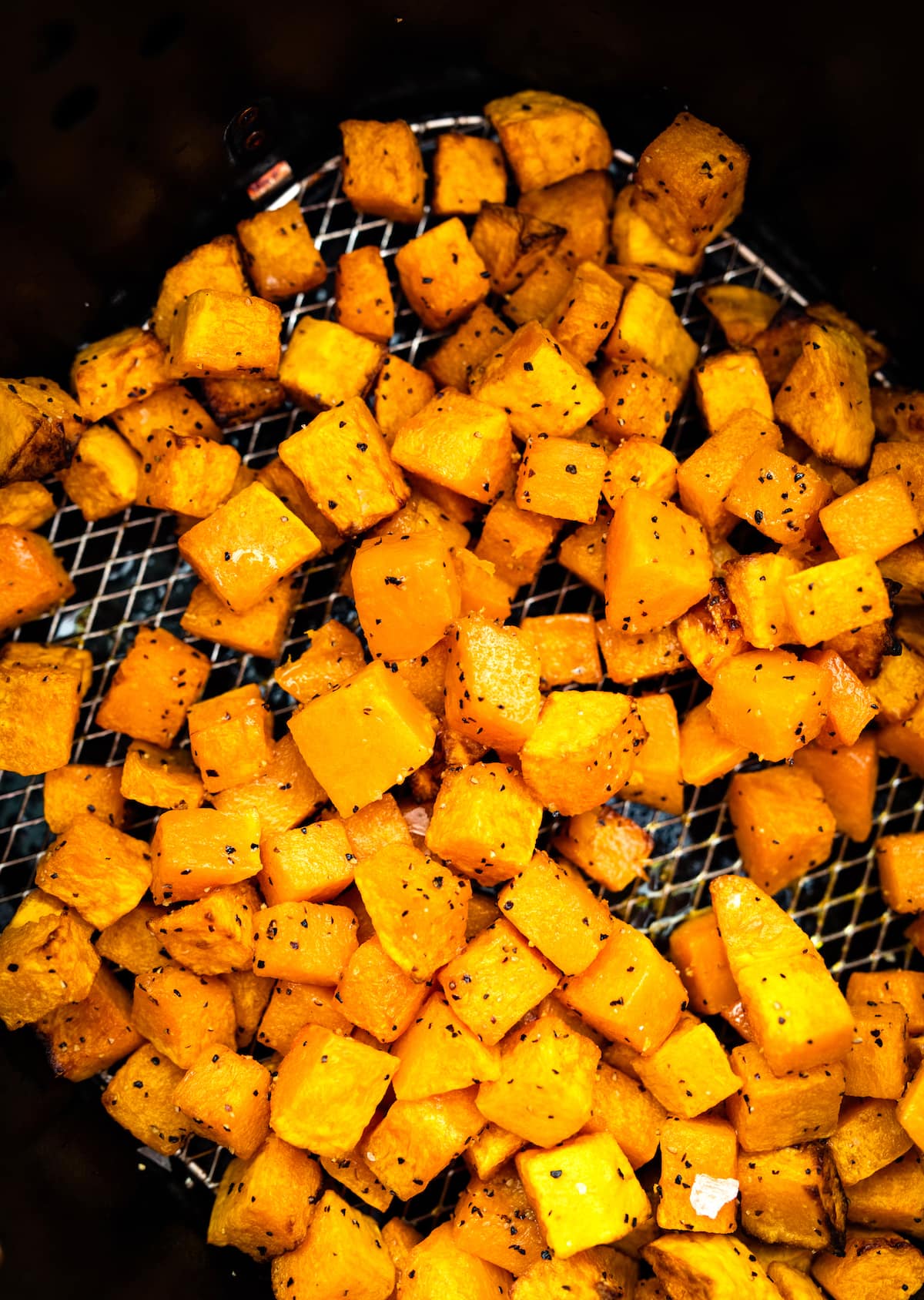 Cubed butternut squash that has been seasoned and is sitting in an air fryer basket in an air fryer.