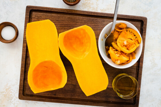 A butternut squash cut in half on a wooden cutting board that has been deseeded.