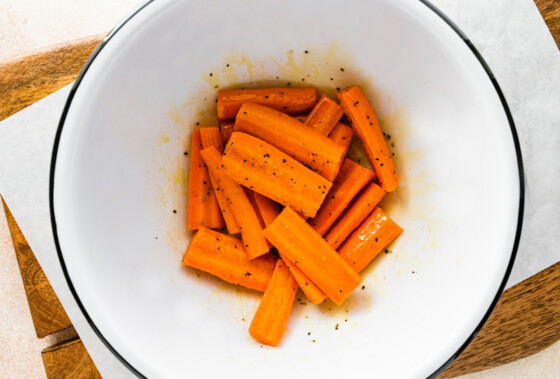Matchstick carrots in a large mixing bowl with seasoning and oil.