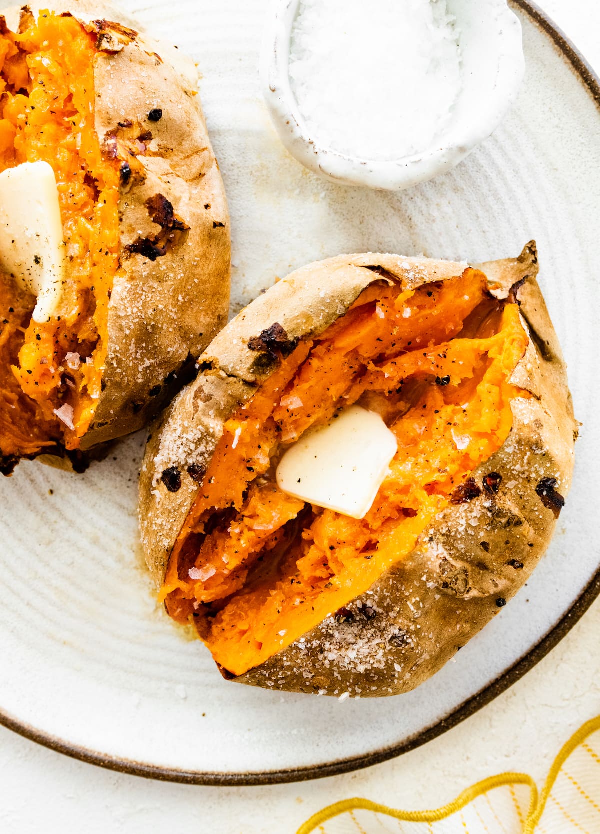 Split open, air fried sweet potato on a plate with a slice of butter.