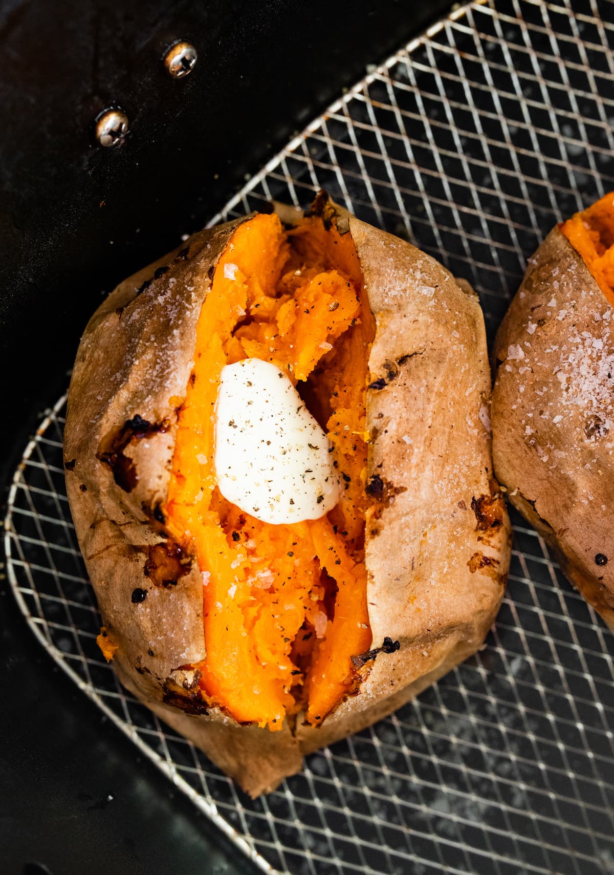 A whole sweet potato split in half with butter in the middle. The sweet potato is in an air fryer basket.