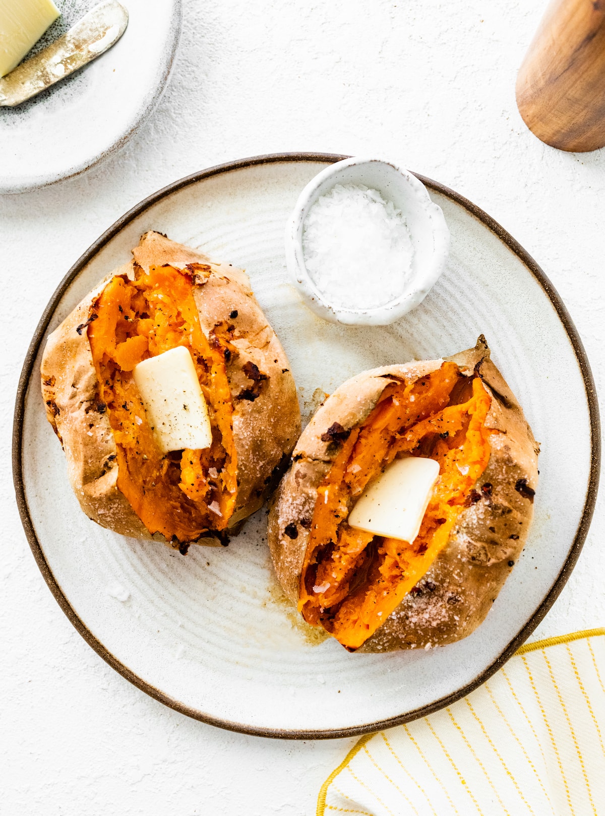 Two whole air-fried sweet potatoes on a plate. The sweet potatoes are split open with a slice of butter inside.