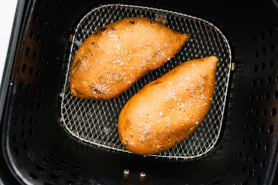 Two whole sweet potatoes with sea salt in an air fryer basket in an air fryer.