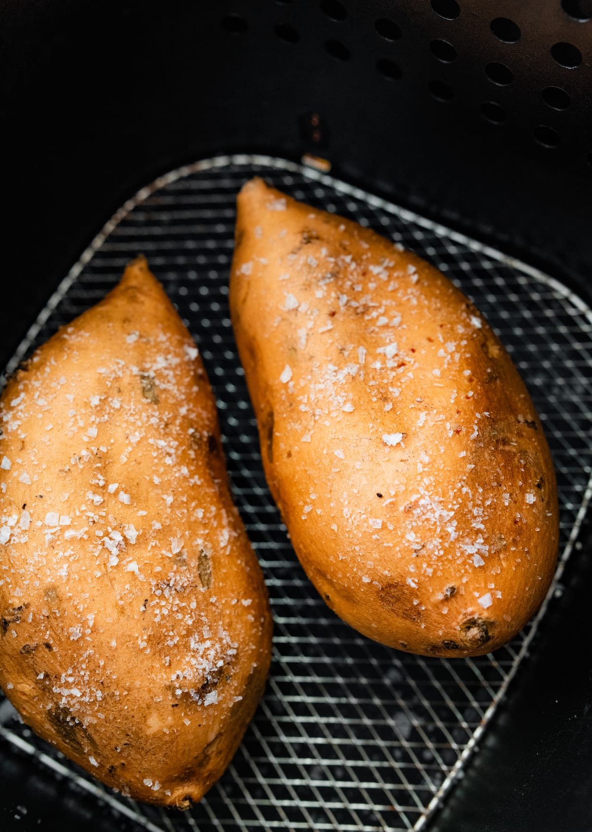 Two whole sweet potatoes with sea salt in an air fryer basket.