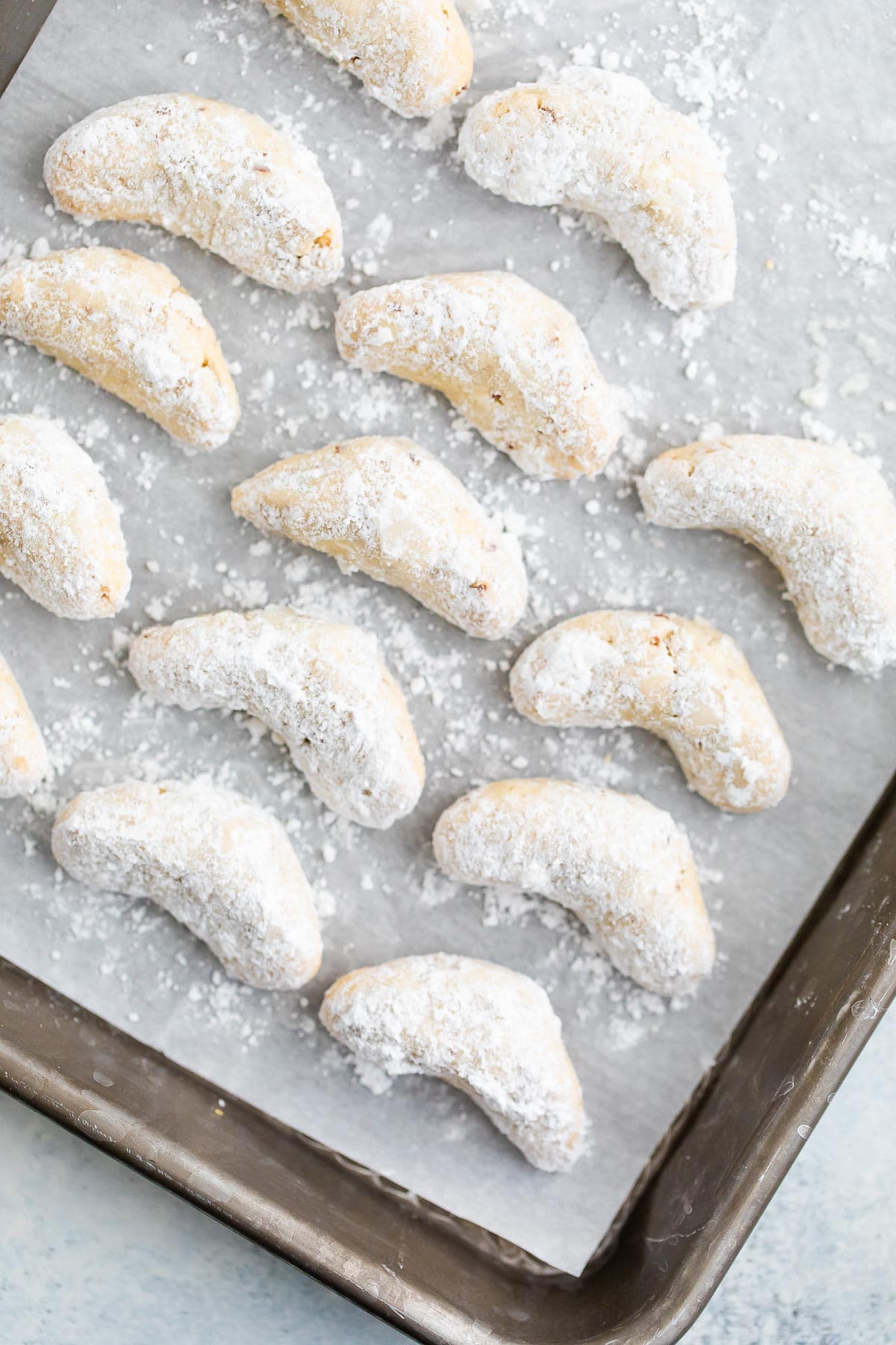 Baked and coated almond crescent cookies on a baking sheet lined with parchment paper.