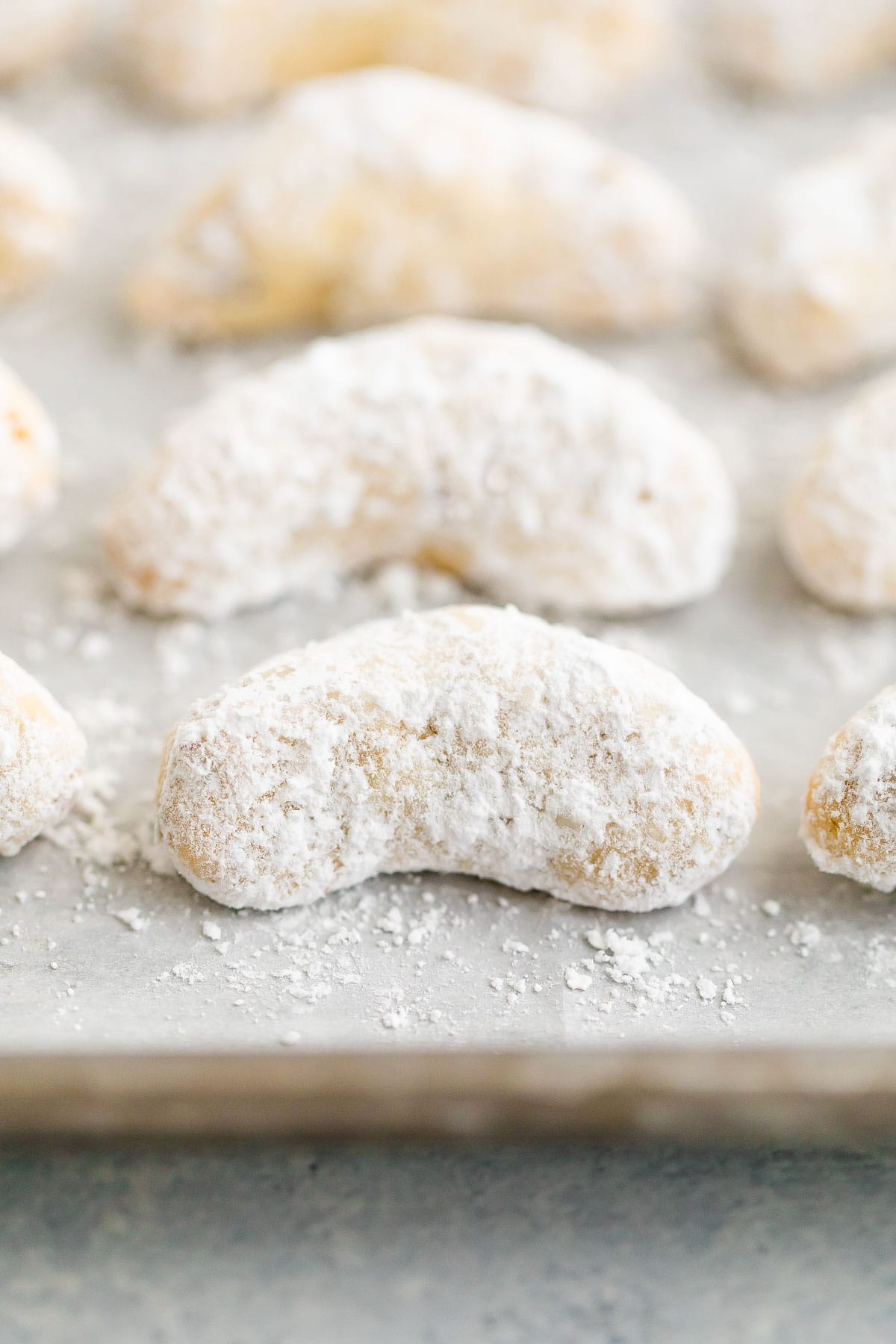 A close up image of almond crescent cookies on a baking sheet with parchment paper.