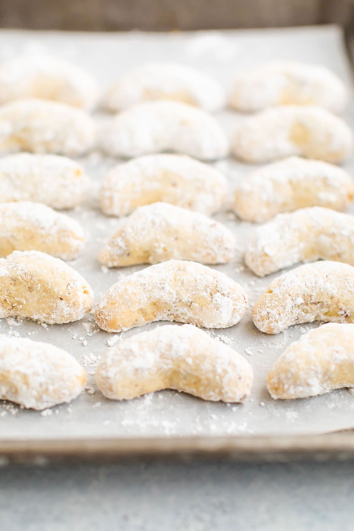Baked and coated almond crescent cookies on a baking sheet lined with parchment paper.
