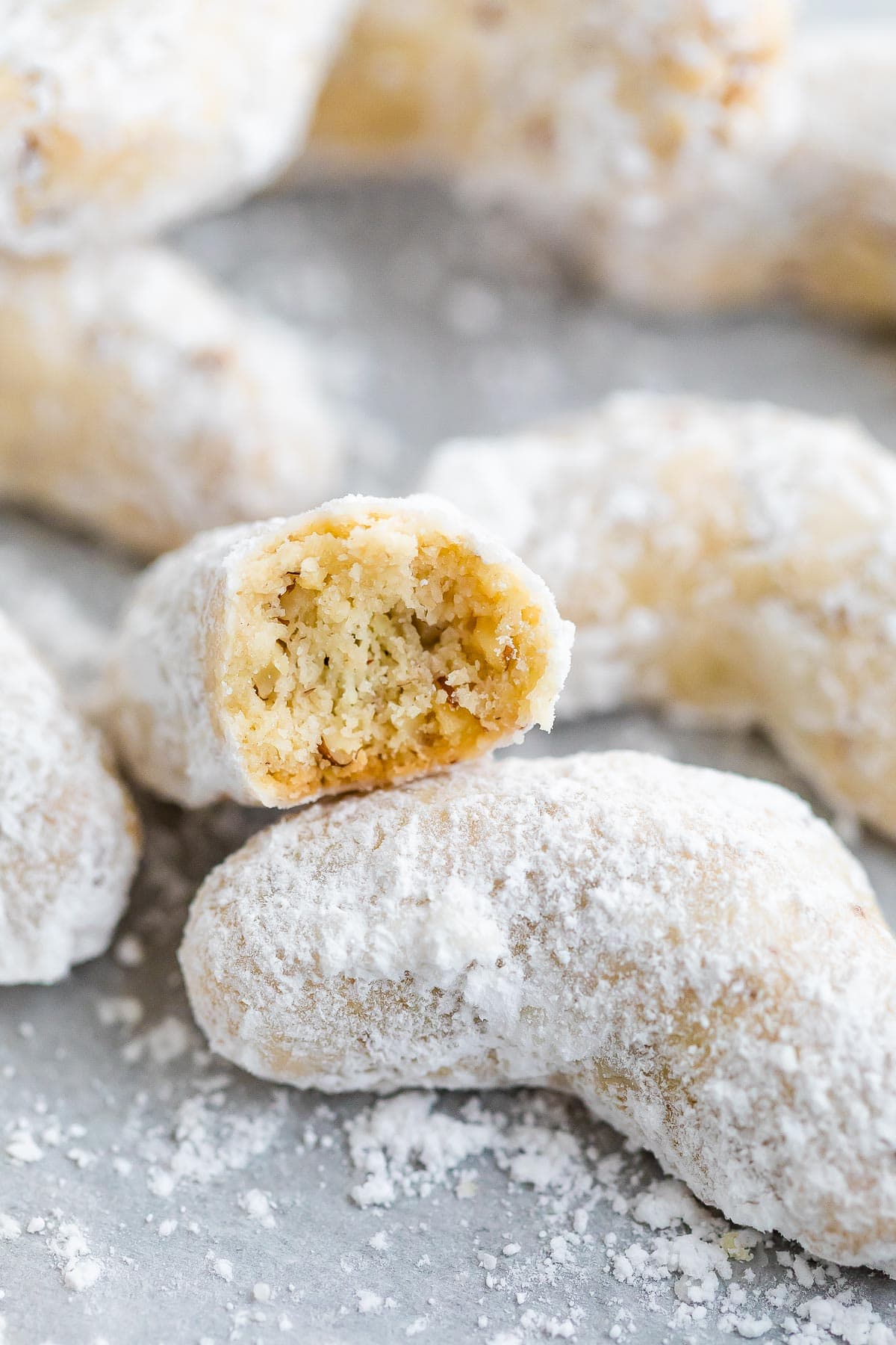 Almond crescent cookies on parchment paper with one bite taken out of one of the cookies.