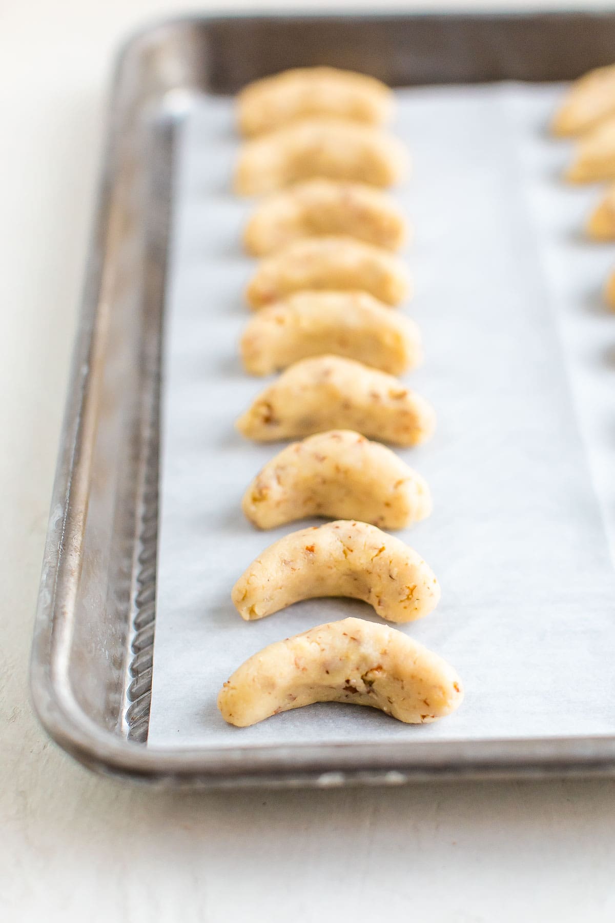 Unbaked almond crescent cookies on a baking sheet lined with parchment paper.
