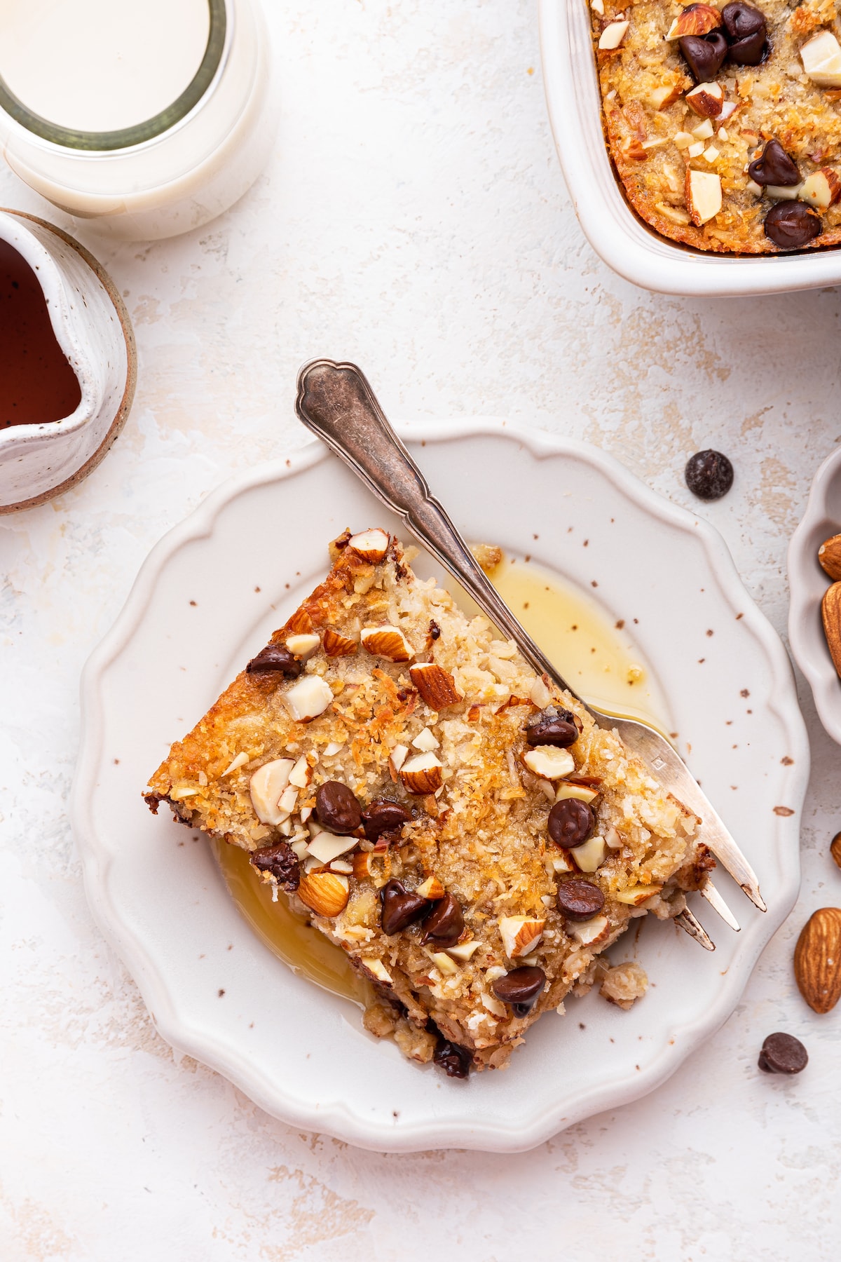 A serving of almond joy baked oatmeal on a small plate with maple syrup and a metal fork.