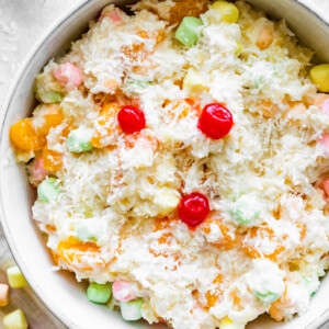 Ambrosia salad in a large bowl topped with shredded coconut, cherries, and mini marshmallows.