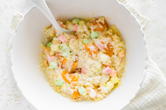 All the ingredients for the ambrosia salad mixed in a large bowl with a serving spoon.