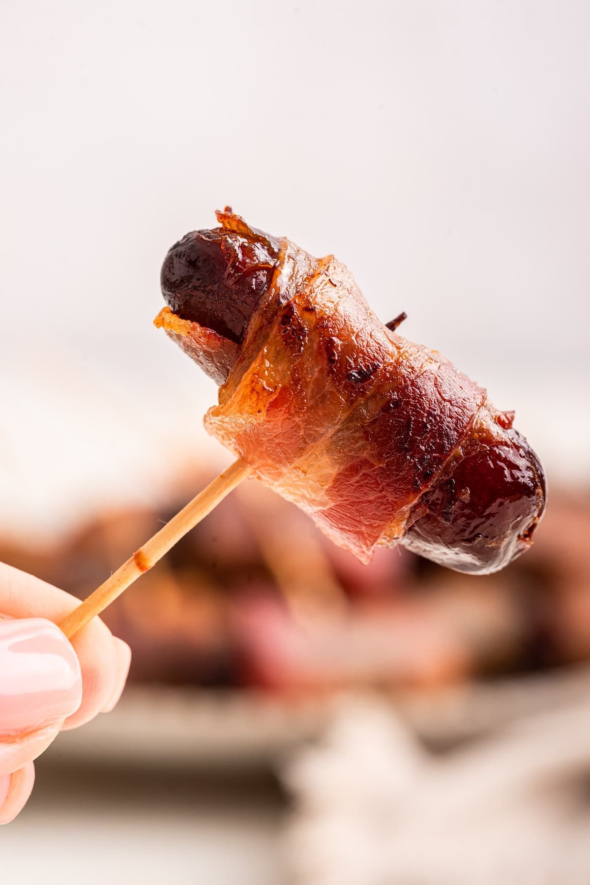 A woman's hand holding a toothpick with a bacon wrapped date.