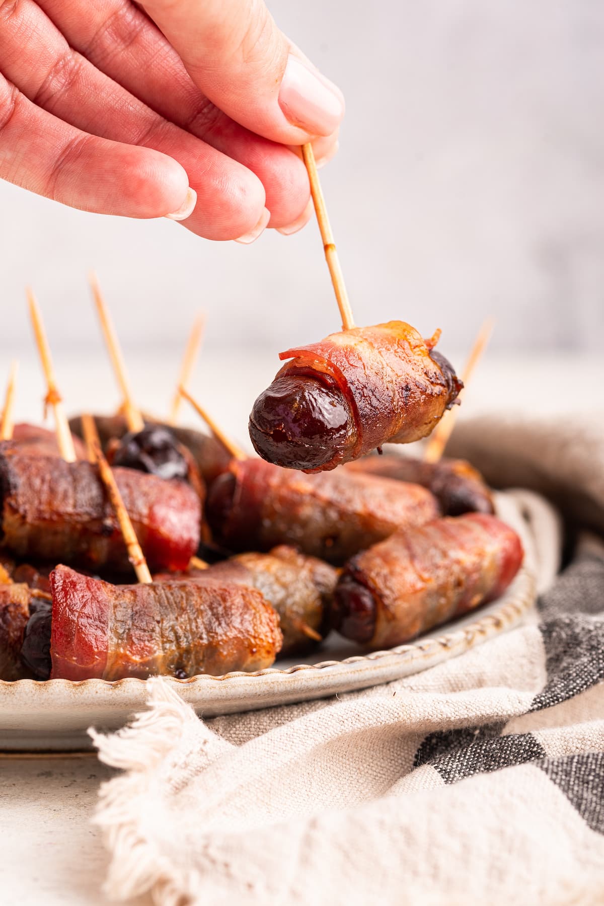 A woman's hand holding a toothpick with a bacon wrapped date.
