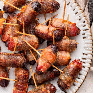 Bacon wrapped dates with toothpicks going through them on a plate.