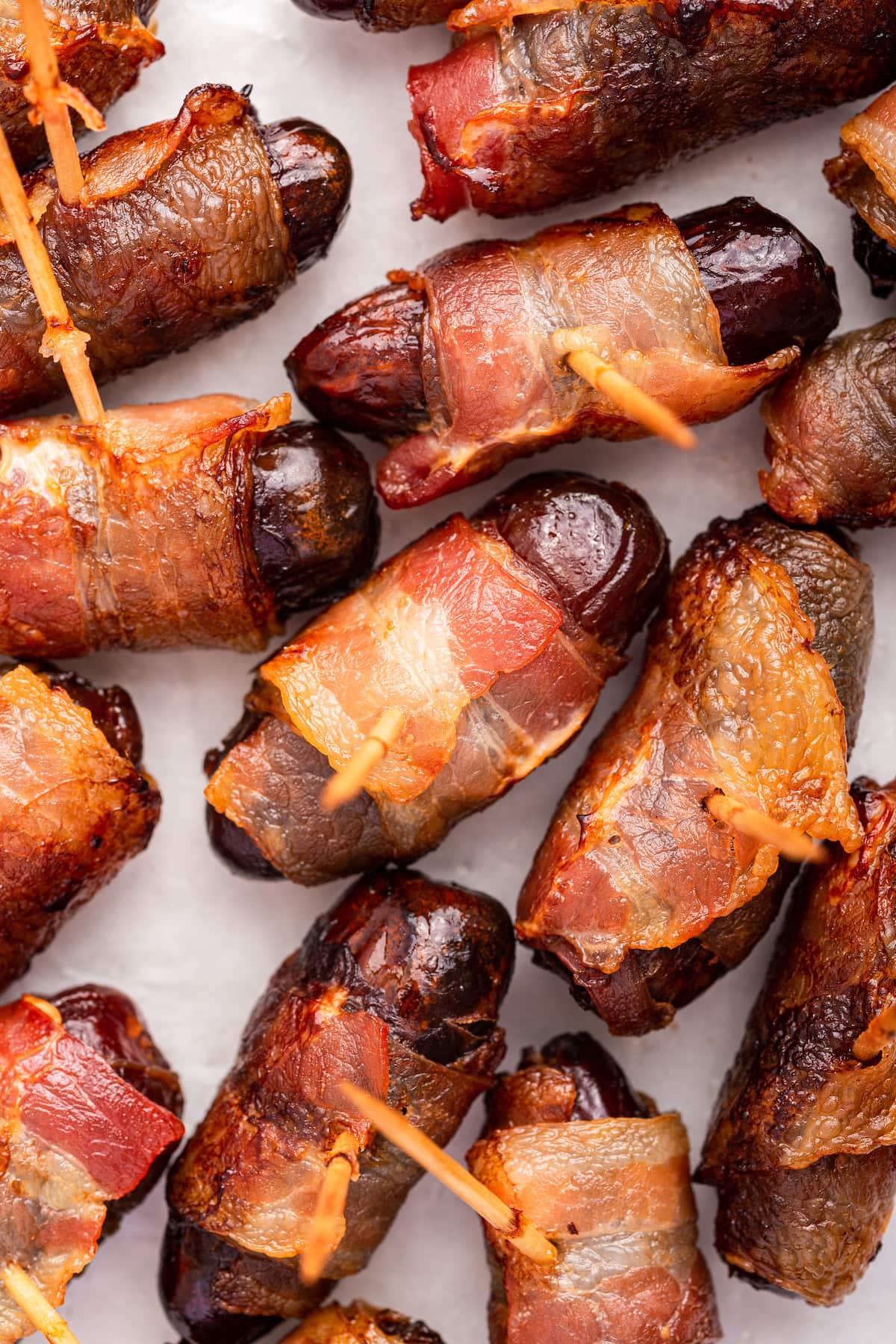 Bacon wrapped dates with toothpicks going through them on a plate.