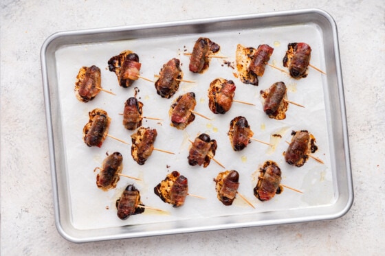 Multiple dates wrapped in bacon on a baking sheet after being baked in the oven.