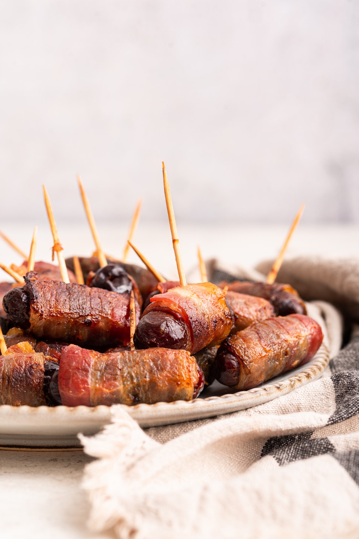 Bacon wrapped dates with toothpicks going through them on a plate.