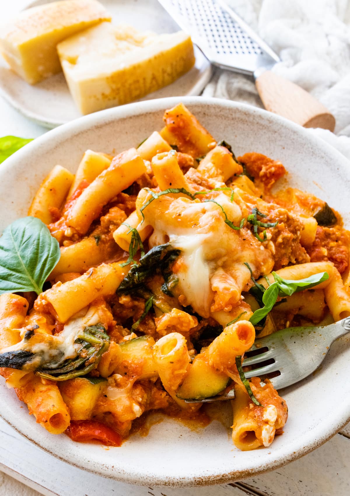 A serving of baked ziti on a small plate with a metal fork.