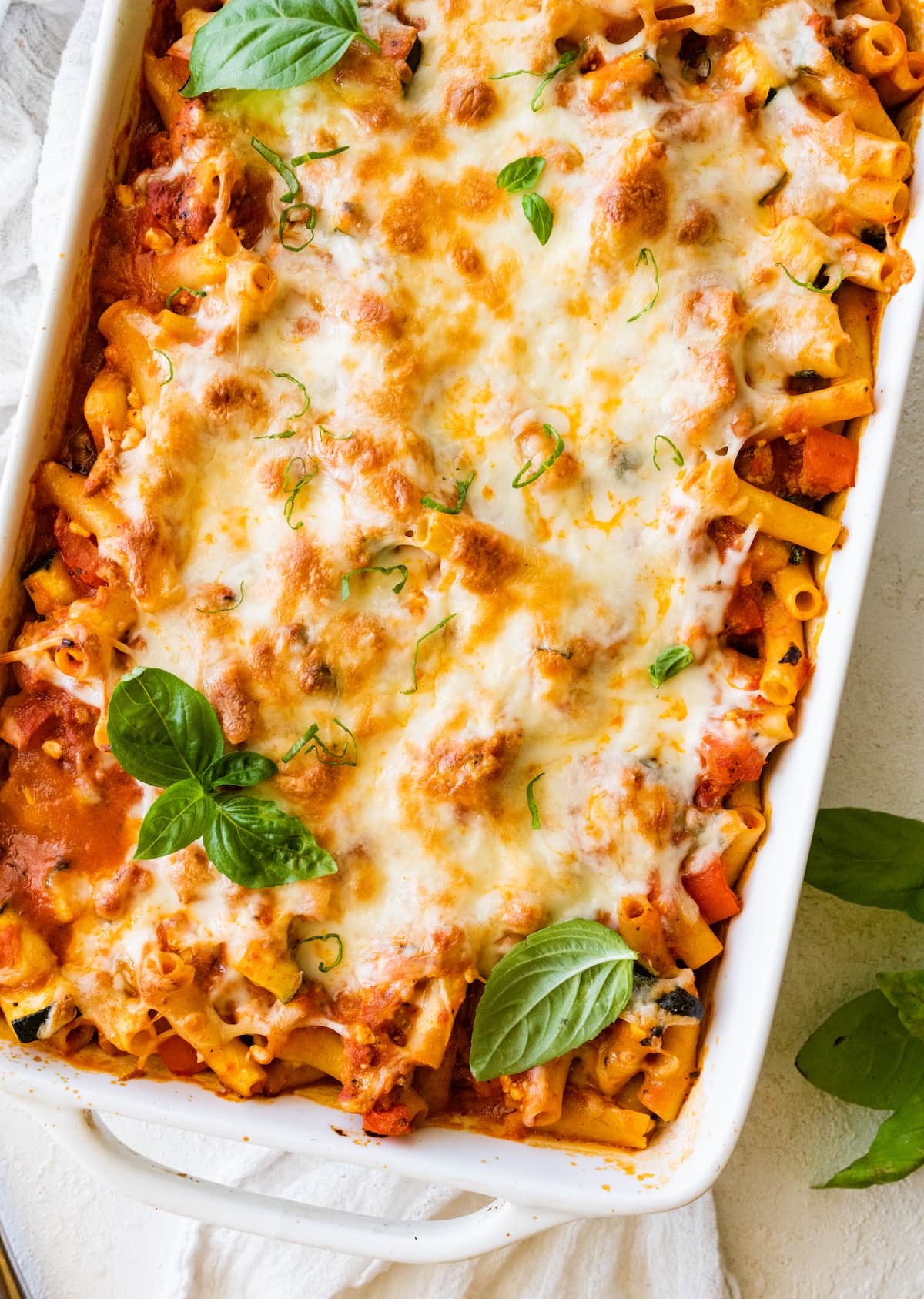 A large square baking dish with baked ziti and fresh basil as a garnish.