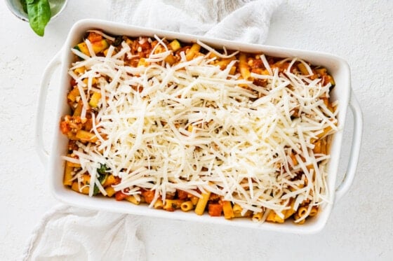 Shredded mozzarella cheese added to the top of the pasta noodles and turkey tomato sauce in a large square baking dish.