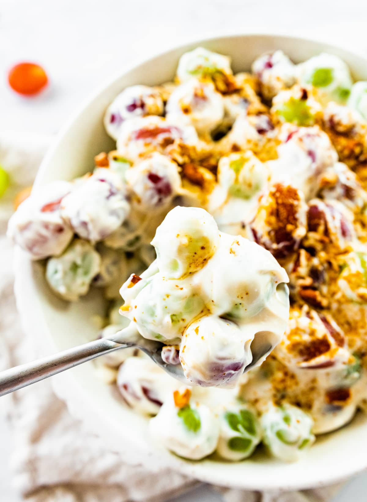 A serving of creamy grape salad on a spoon above a large bowl of the salad.