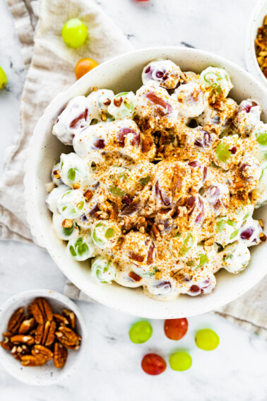 Creamy grape salad topped with sugar and crushed pecans in a large bowl.