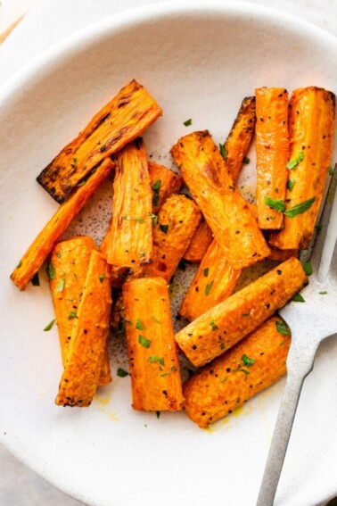 Air fried carrots cut into matchsticks on a plate and garnished with fresh herbs.