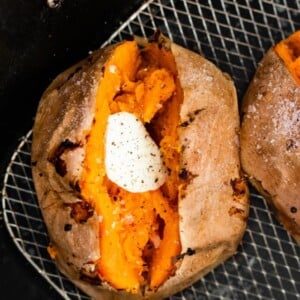 A whole sweet potato split in half with butter in the middle. The sweet potato is in an air fryer basket.