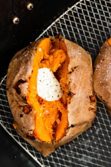 A whole sweet potato split in half with butter in the middle. The sweet potato is in an air fryer basket.