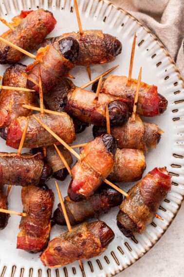 Bacon wrapped dates with toothpicks going through them on a plate.