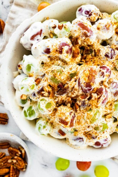 Creamy grape salad topped with sugar and crushed pecans in a large bowl.