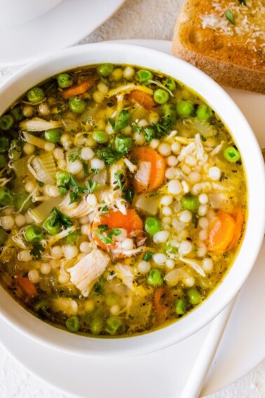 Leftover turkey soup in a bowl with multiple vegetables, including peas, carrots, and onions.