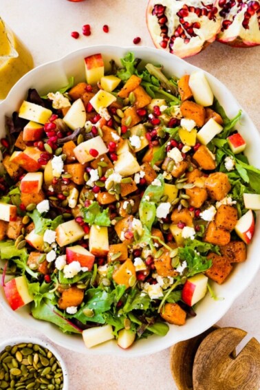 A large bowl of Thanksgiving salad with some noticeable ingredients including pomegranate, diced apple, spinach, pumpkin seeds, and more.