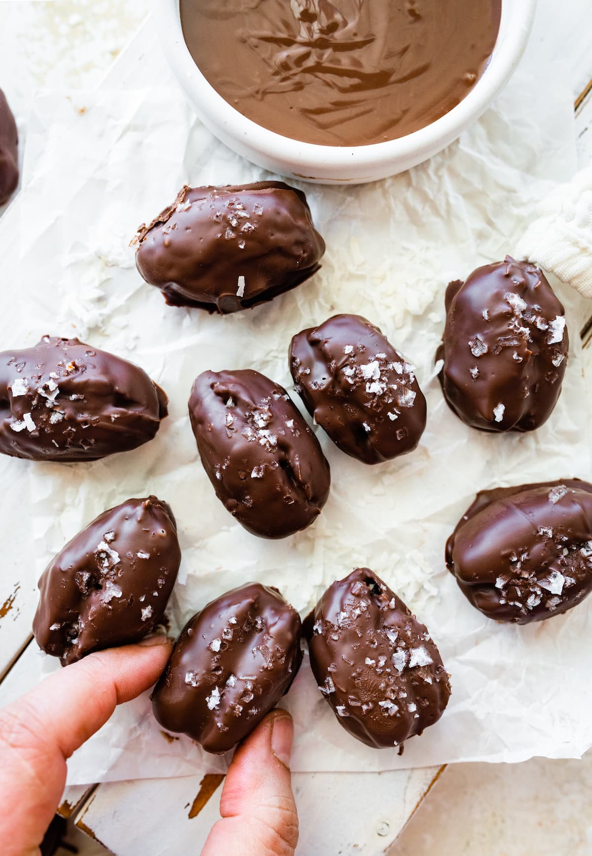 Multiple date mounds bars on parchment paper with a woman's hand grabbing one.