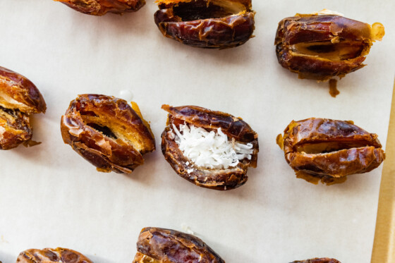 Multiple Medjool dates on a baking tray with one filled with coconut butter and coconut flakes.