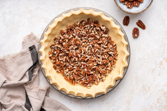 Chopped pecans in the bottom of a pie crust in a prepared pie dish.