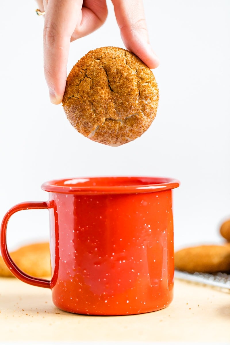 A woman's hand holding a gluten-free snickerdoodle cookie over a red mug.