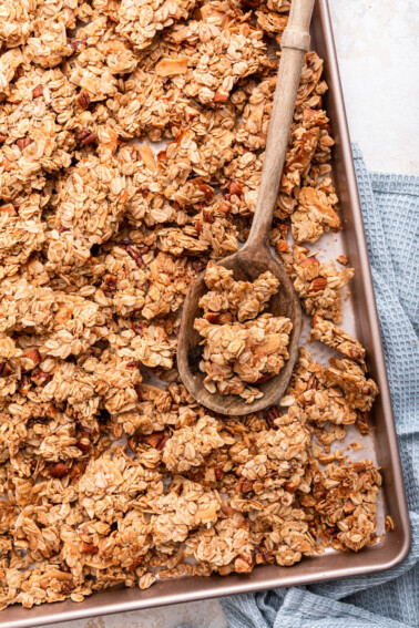 Homemade granola on a baking sheet with a wooden serving spoon.